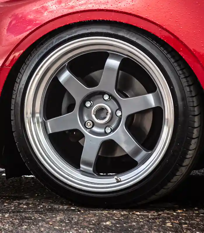 Gunmetal 6-Spoke Rim on Red Car | Automotive Expressions Automotive Expressions custom six-spoke gunmetal alloy wheel with polished lip on red car, low-profile tire on wet pavement