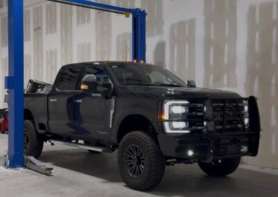 Automotive Expressions black lifted Ford Super Duty with grille guard, LED lights, off-road tires in shop by blue 2-post lift