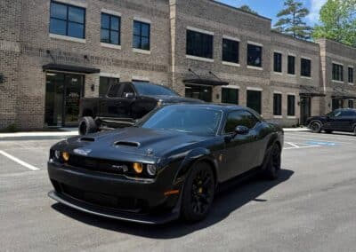 Automotive Expressions black Dodge Challenger Hellcat with amber halos at brick offices; truck in background, auto styling
