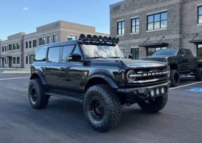 Black lifted Ford Bronco with roof LED pods, bumper lights and oversized off-road tires at Automotive Expressions lot