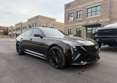 Automotive Expressions black Cadillac sedan, gloss black multi-spoke wheels, red calipers, parked by brick office buildings