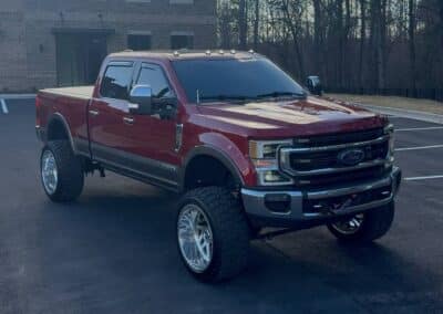 Lifted red Ford Super Duty with polished deep-dish wheels, offroad tires, and dark tint—Automotive Expressions custom truck