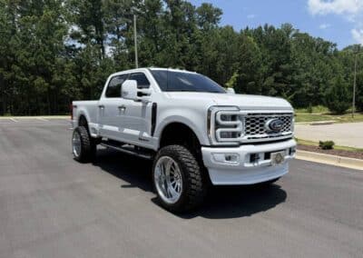 White lifted Ford Super Duty with custom lift, deep-dish alloy wheels and off-road tires on asphalt - Automotive Expressions