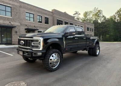 Automotive Expressions lifted black Ford Super Duty dually with chrome dually wheels, mud-terrain tires by a brick office